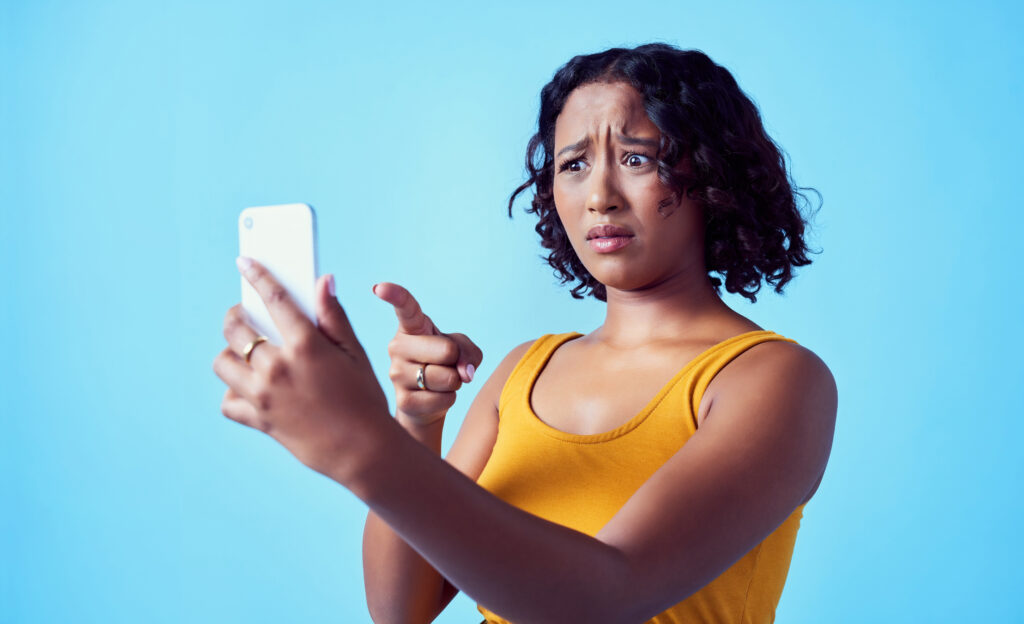 A woman stares at her phone, pointing at the screen in frustration.